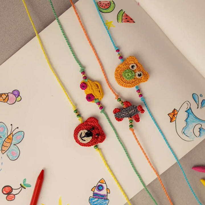 Handmade Crochet Toys And Animals Theme Kids Rakhi With Roli Chawal Set Of 4 - Displayed with Children's Drawing Background