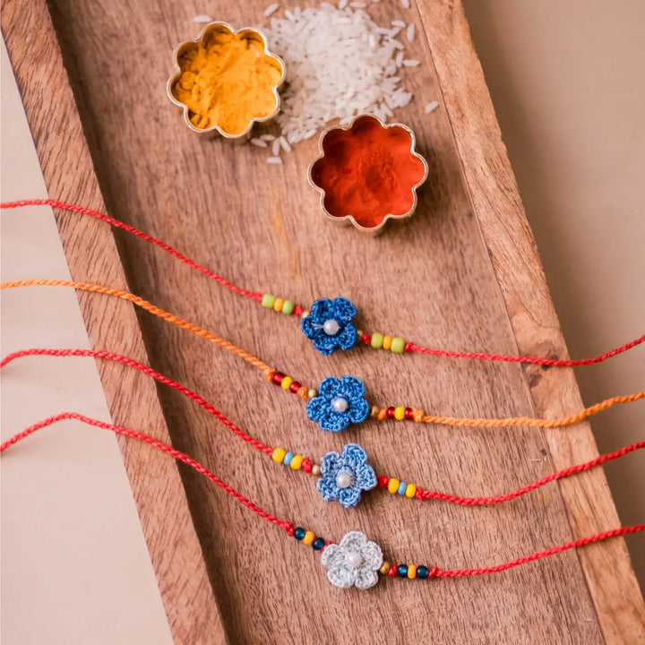 Handmade Crochet Pink Daisies Rakhi With Roli Chawal Set Of 4 - Top view with blue flower bracelets and spices
