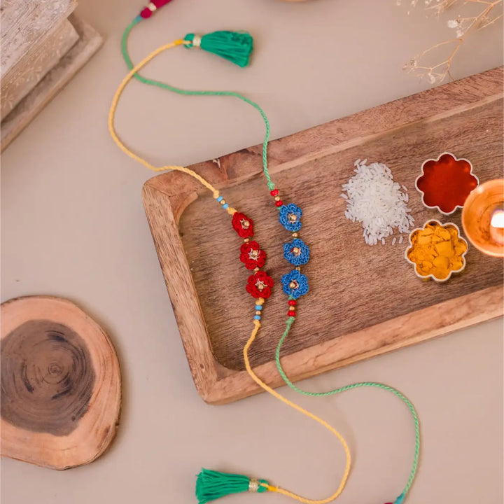 Handmade Crochet Red And Blue Floral Rakhi With Roli Chawal Set Of 2 - Full Length with Decorative Background