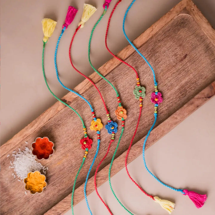 Handmade Crochet Multicolor Daisies Rakhi With Roli Chawal Set Of 6 - Overhead view with tassels visible
