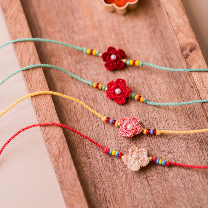 Handmade Crochet Pink Daisies Rakhi With Roli Chawal Set Of 4 - Top view with red and peach flower bracelets and spices