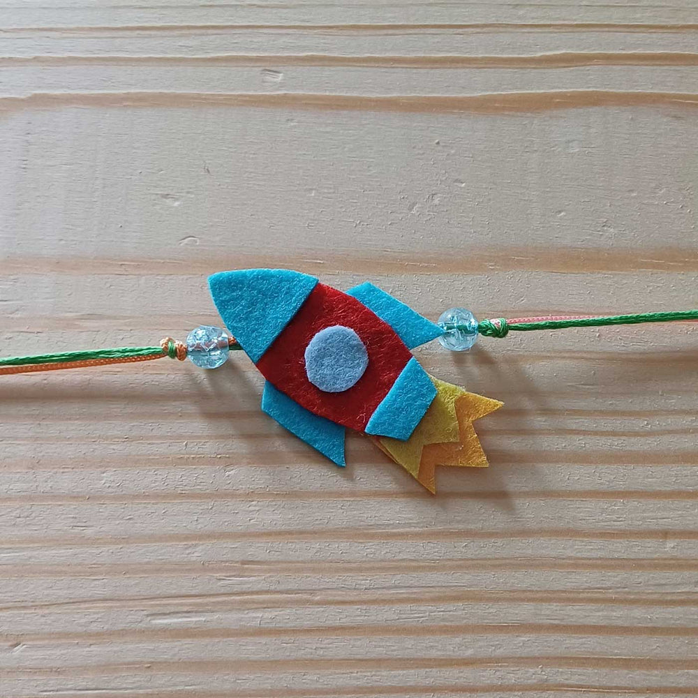 Handmade Rocket Theme Felt Kids Rakhi - Flat Lay on Wooden Surface