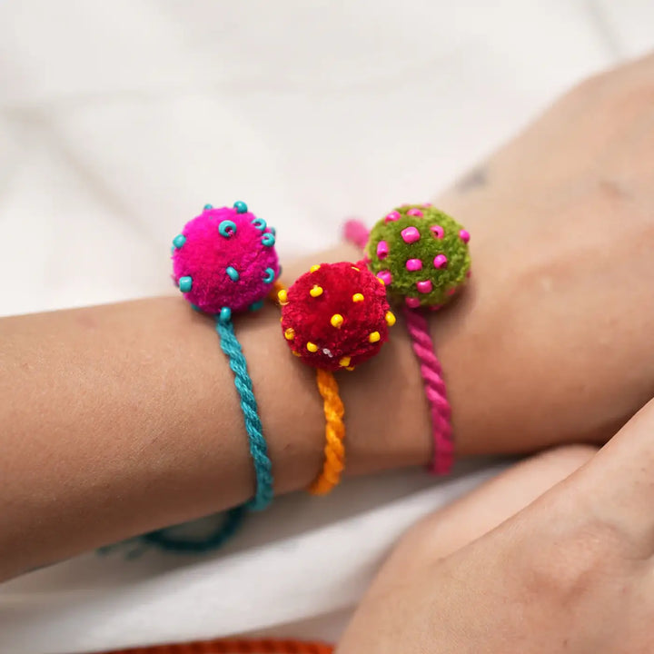 Handmade Embroidered And Beaded Mini Laddoo And Aaina Rakhi With Roli Chawal Set Of 5 - Close-up of pom pom bracelets