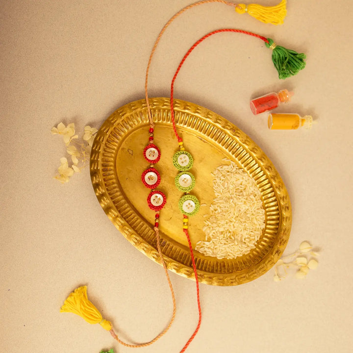 Handmade Crochet Ananta Rakhi With Roli Chawal Set Of 2 - Flat lay with mixed bracelet colors