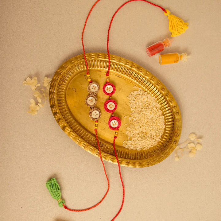 Handmade Crochet Ananta Rakhi With Roli Chawal Set Of 2 - Flat lay with brass tray and powder bottles