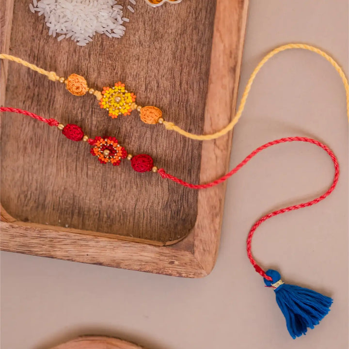 Handmade Crochet Red And Yellow Flower Rakhi With Roli Chawal Set Of 2 - Top View with Tassels Displayed