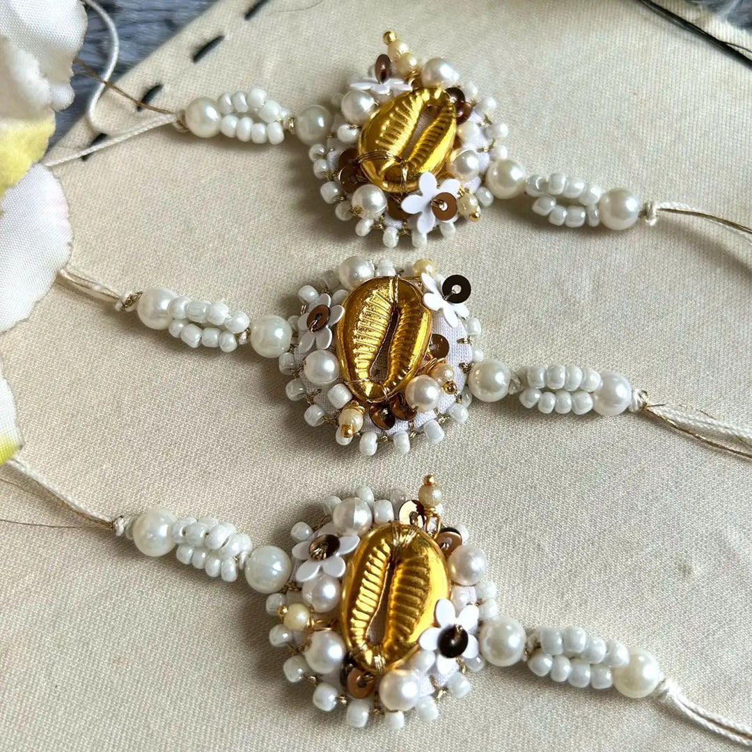 Hand Embroidered Beaded White And Golden Shell Rakhi With Roli Chawal Set Of 3 - Close-up of Three Bracelets
