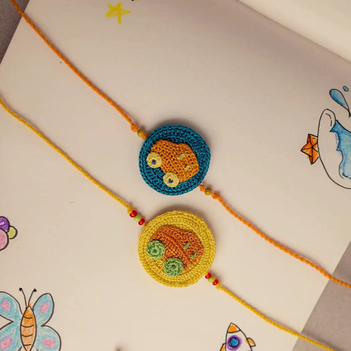 Handmade Crochet Playful Cars Theme Kids Rakhi With Roli Chawal Set Of 2 - Top view with drawn background