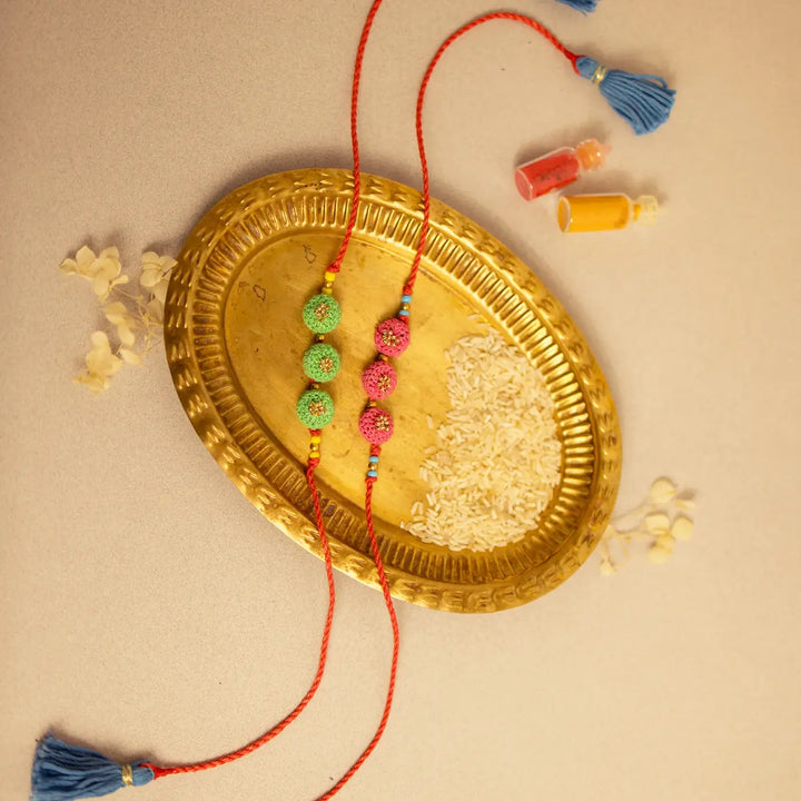 Handmade Crochet Round Ananta Rakhi With Roli Chawal Set Of 2 - Overhead view with colored powders