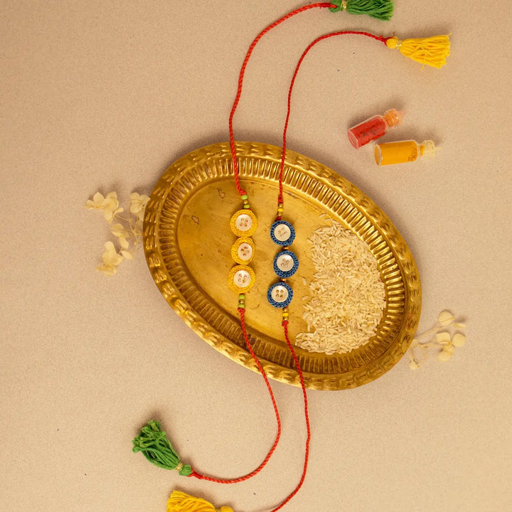 Handmade Crochet Ananta Rakhi With Roli Chawal Set Of 2 - Flat lay with blue and yellow bracelets