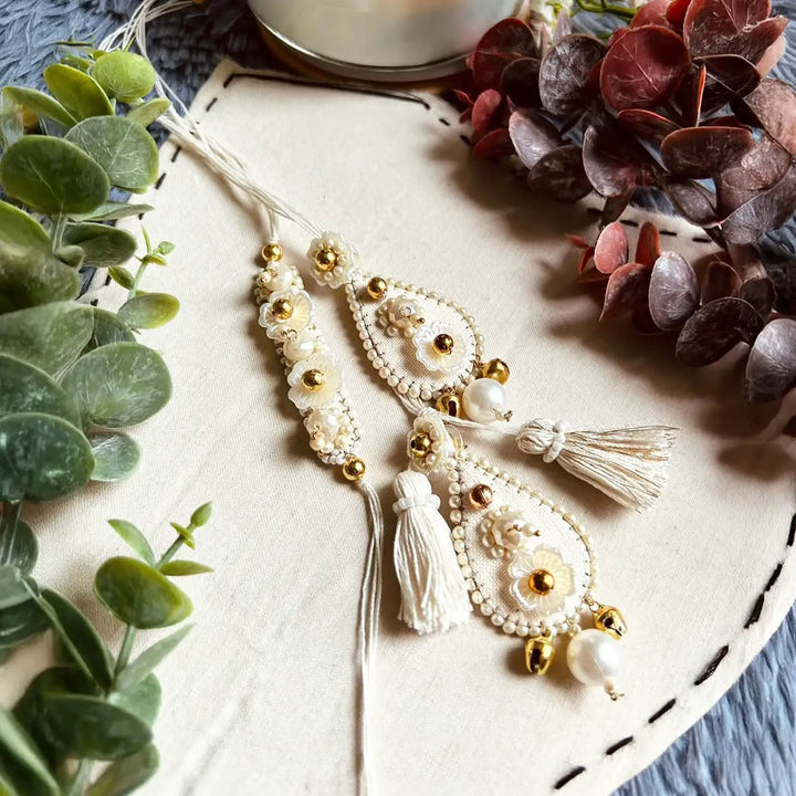 Hand Embroidered Beaded Ivory Bhaiya Bhabhi Rakhi With Roli Chawal Set Of 2 - Top View with Decorative Plants