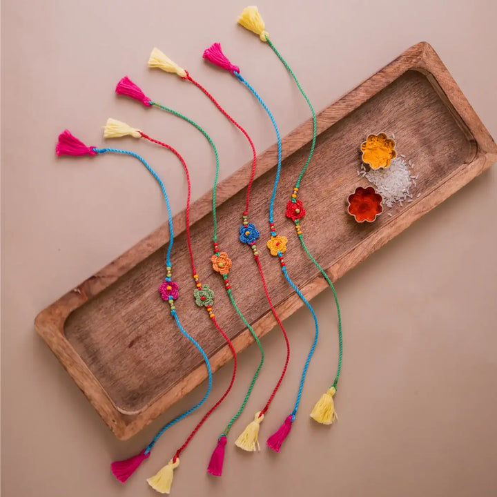 Handmade Crochet Multicolor Daisies Rakhi With Roli Chawal Set Of 6 - Flat lay with wooden tray