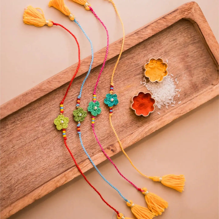 Handmade Crochet Pink Daisies Rakhi With Roli Chawal Set Of 4 - Flat lay of blue flower bracelets with spices