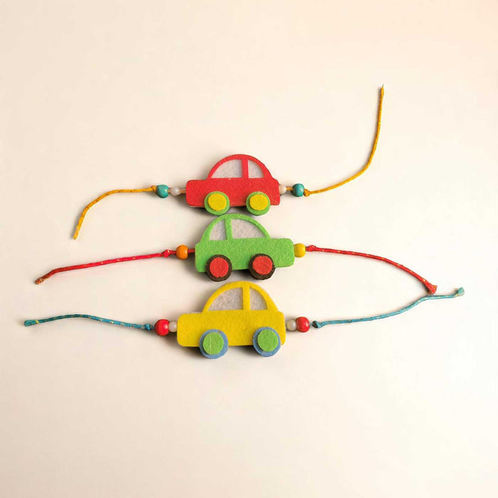 Customized Handmade Beaded Car Theme Pom Pom Felt Rakhi With Roli Chawal For Kids - Three Car Bracelets on Plain Background