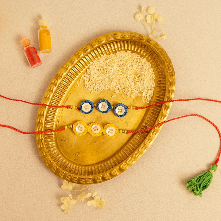 Handmade Crochet Ananta Rakhi With Roli Chawal Set Of 2 - Flat lay display with loose rice and tassels