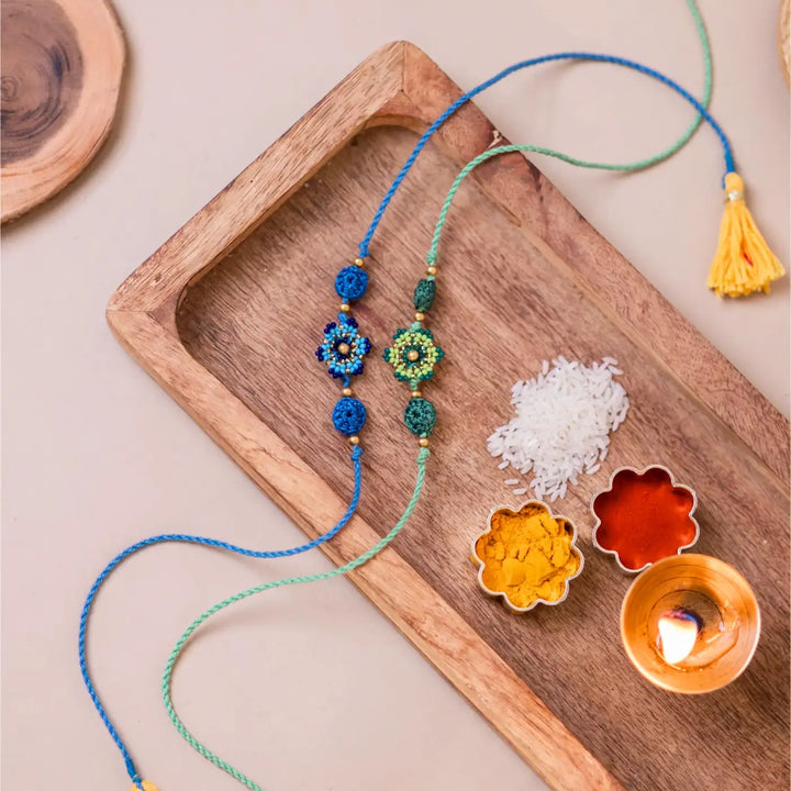 Handmade Crochet Blue And Green Flower Rakhi With Roli Chawal Set Of 2 - Styled Flat Lay with Decorative Items