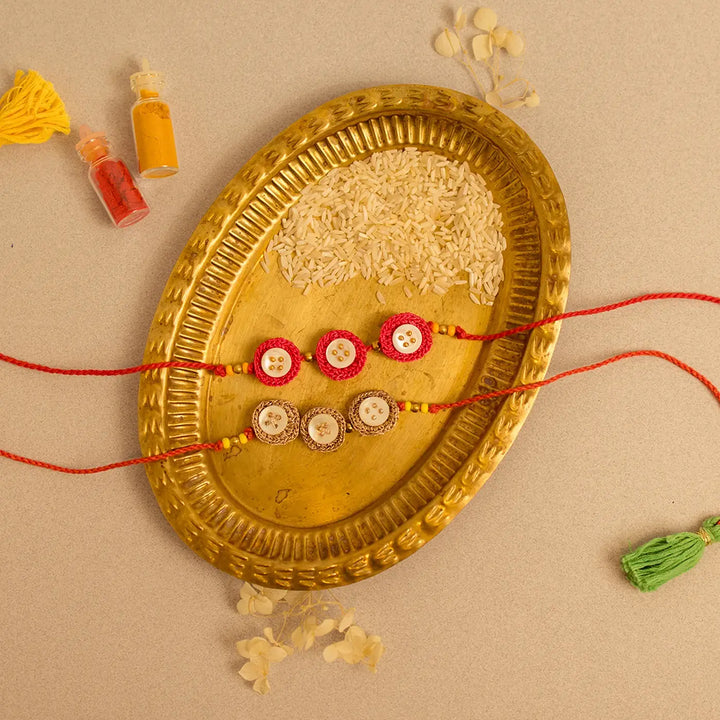 Handmade Crochet Ananta Rakhi With Roli Chawal Set Of 2 - Flat lay of bracelets with rice in tray