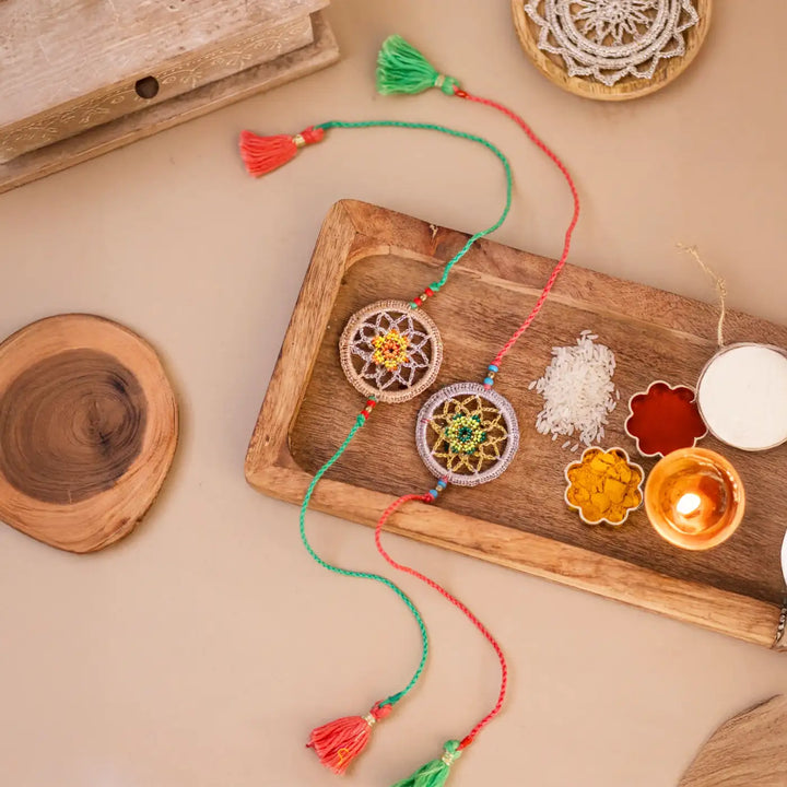 Handmade Crochet Dreamcatcher Rakhi With Roli Chawal Set Of 2 - Ritual setup with bracelets and candles
