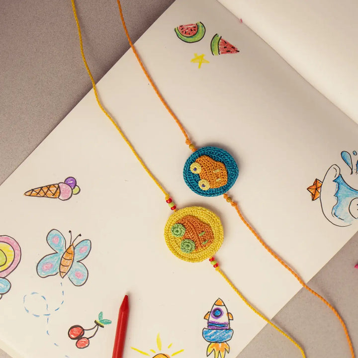Handmade Crochet Playful Cars Theme Kids Rakhi With Roli Chawal Set Of 2 - Angled view with drawings and beads