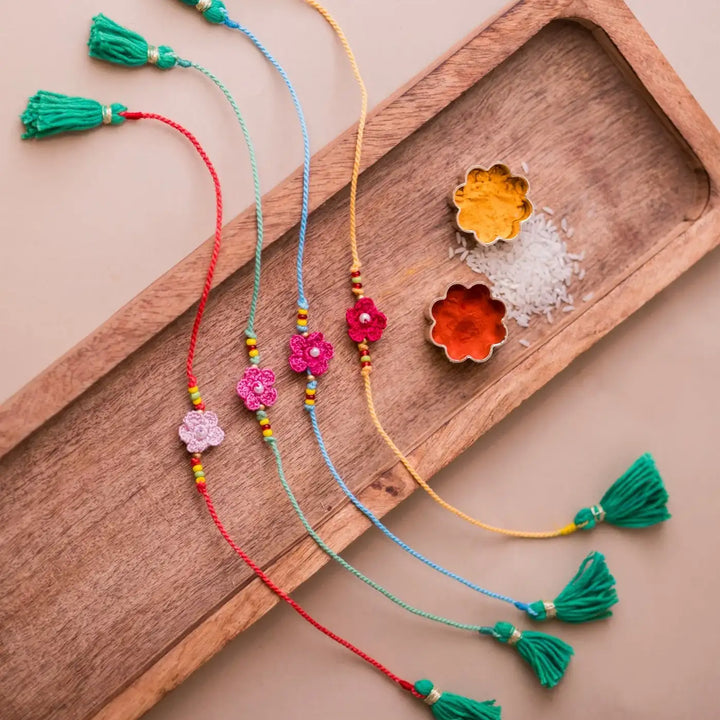 Handmade Crochet Pink Daisies Rakhi With Roli Chawal Set Of 4 - Top angle with bracelets and decorative bowls