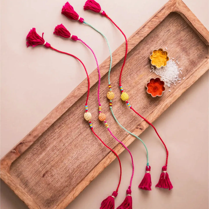 Handmade Crochet Yellow Beads Rakhi With Roli Chawal Set Of 4 - Full set laid on wooden tray