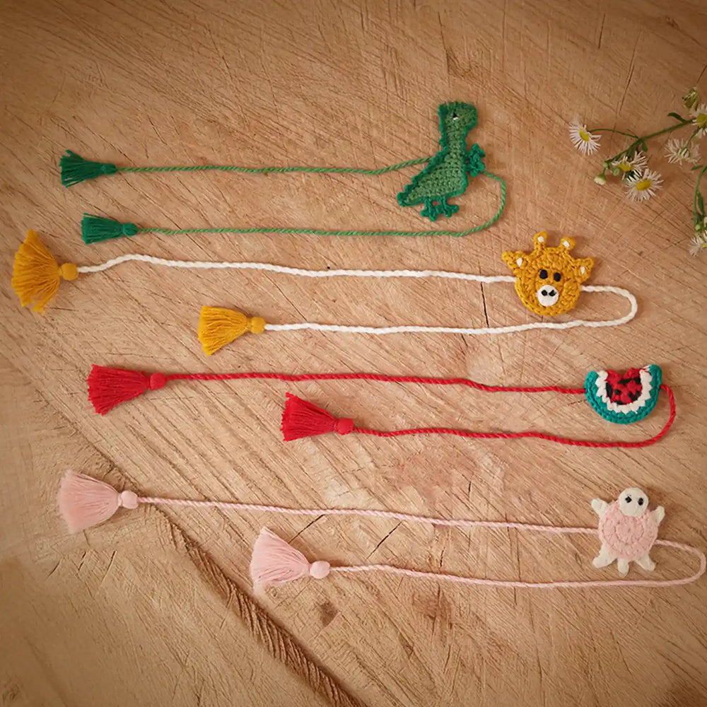 Handmade Crochet Dino Turtle Giraffe And Watermelon Kids Rakhi With Roli Chawal Set Of 4 - Flat Lay with Tassels and Charms