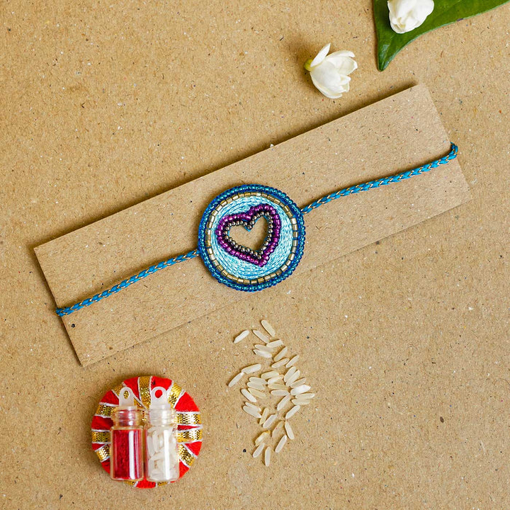 Handmade Beaded Heart Rakhi With Roli Chawal - Bracelet on cardboard with accessories