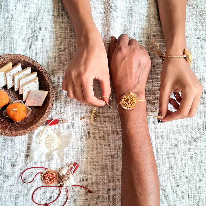Handmade Papier Mache Red And Yellow Swastika Rakhi With Roli Chawal Set Of 2 - Bracelet being tied on wrist