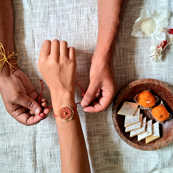 Handmade Papier Mache Red And Yellow Swastika Rakhi With Roli Chawal Set Of 2 - Bracelet being adjusted on wrist