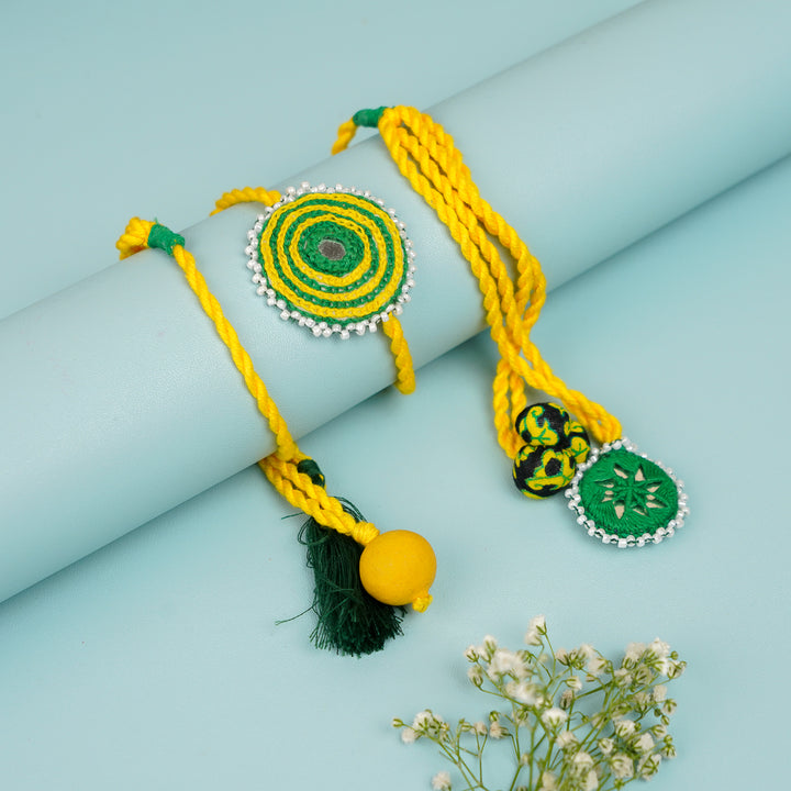 Handmade Reusable Yellow And Green Mirror And Jhumki Cotton Rope Rakhi For Bhabhi - Styled on Cylinder Display