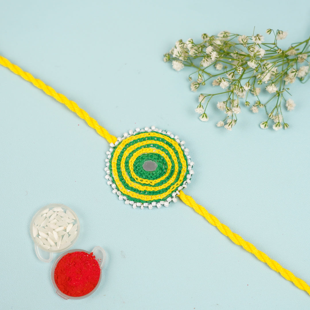 Handmade Reusable Yellow And Green Mirror And Jhumki Cotton Rope Rakhi For Bhabhi - Flat Lay with Accessories