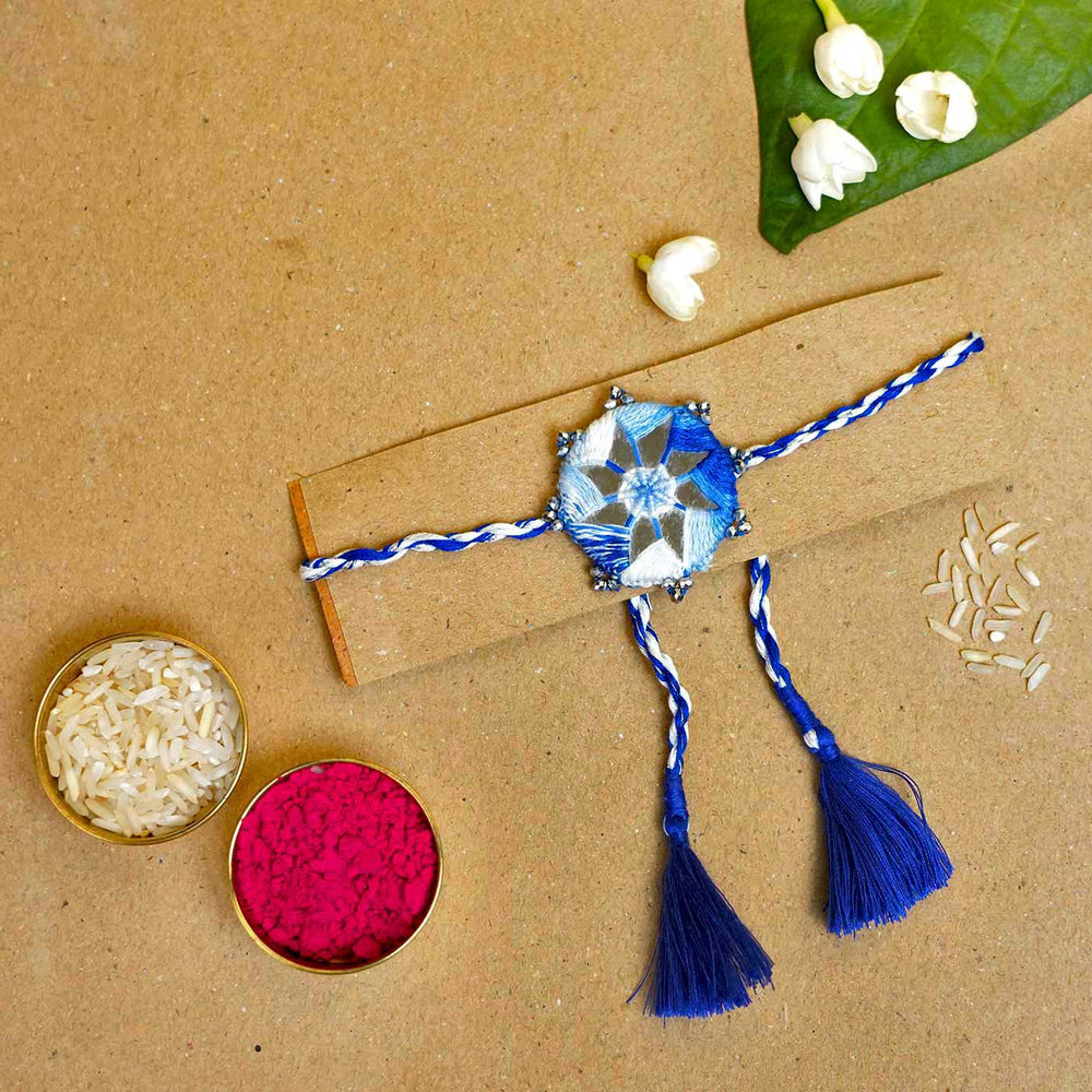 Handmade Mirror Work Kaanha Ombre Blue Cotton Rakhi With Roli Chawal - Flat lay with rice and kumkum