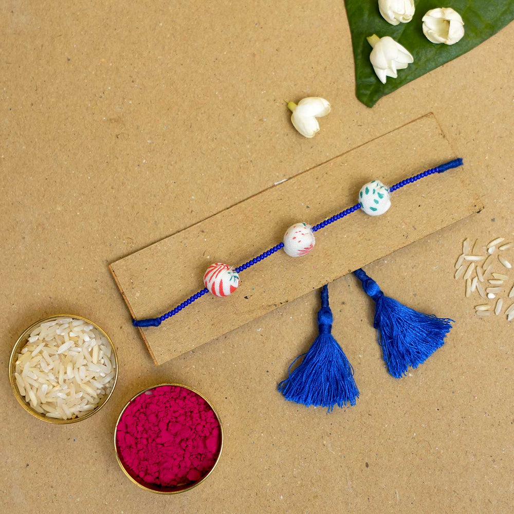 Handmade Shweth Potli Upcycled Fabric Rakhi With Roli Chawal - Bracelet displayed on board