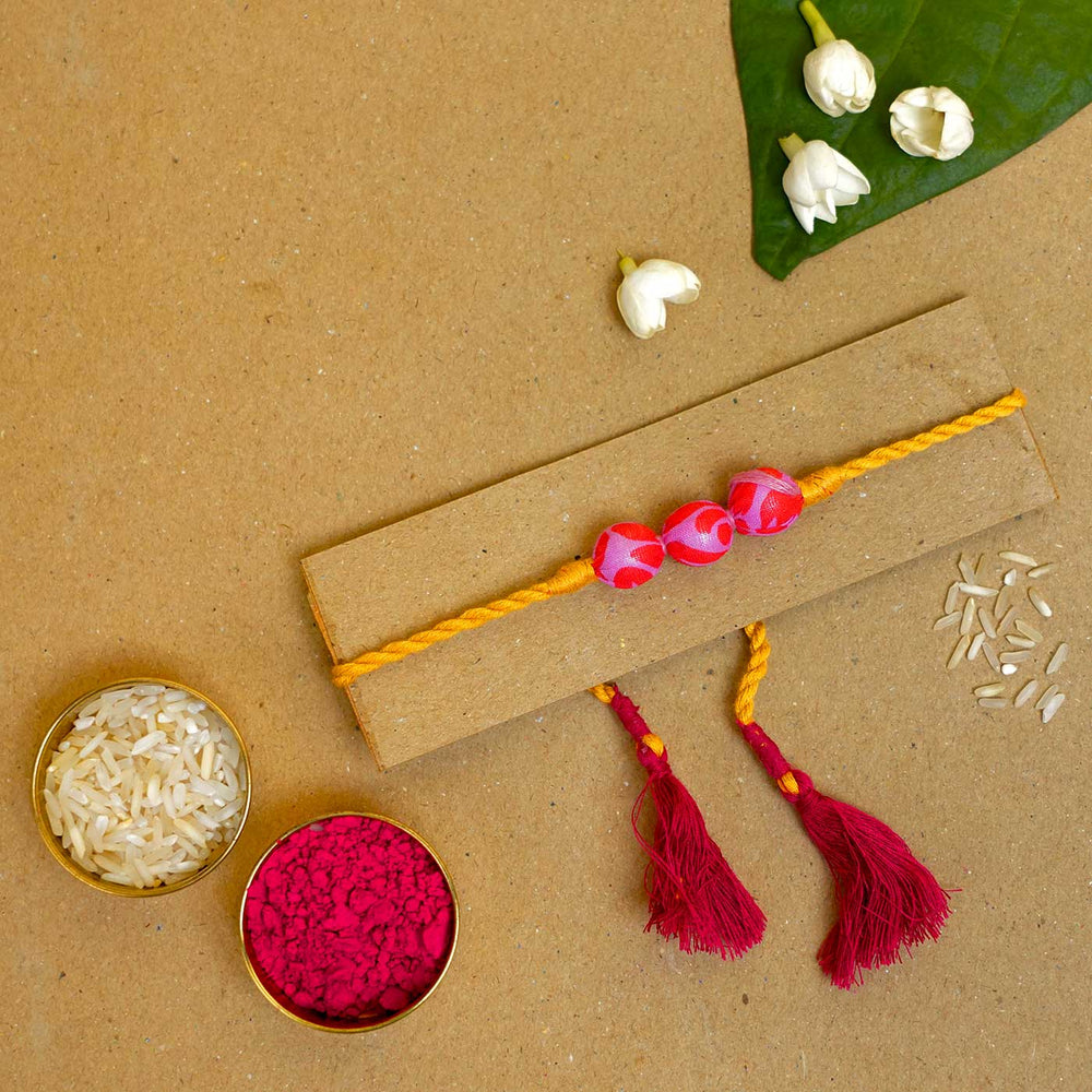 Handmade Pink Yellow Potli Upcycled Fabric Rakhi With Roli Chawal - Styled flat lay with accessories