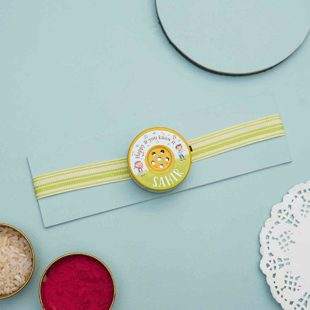 Personalized Musical If Youre Happy And You Know It Kids Rakhi With Roli Chawal - Flat Lay with Ribbon and Small Containers