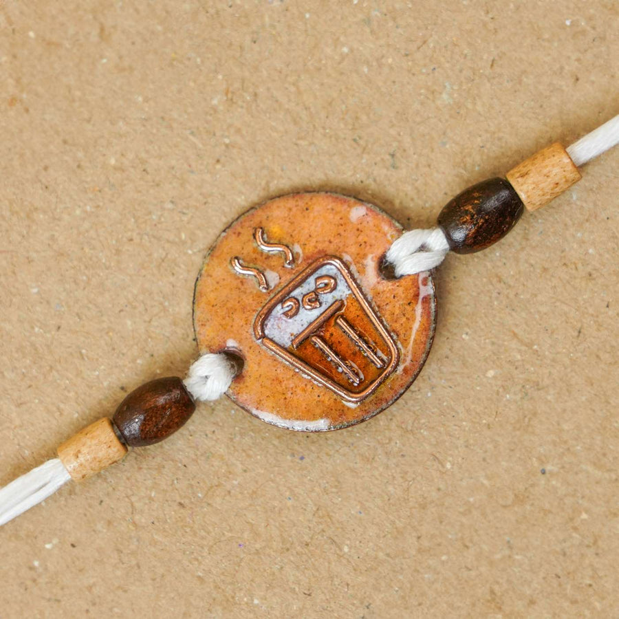 Handmade Chai Paani Brown Copper Enamel Rakhi With Chocolates And Roli Chawal - Close-up of charm and beads