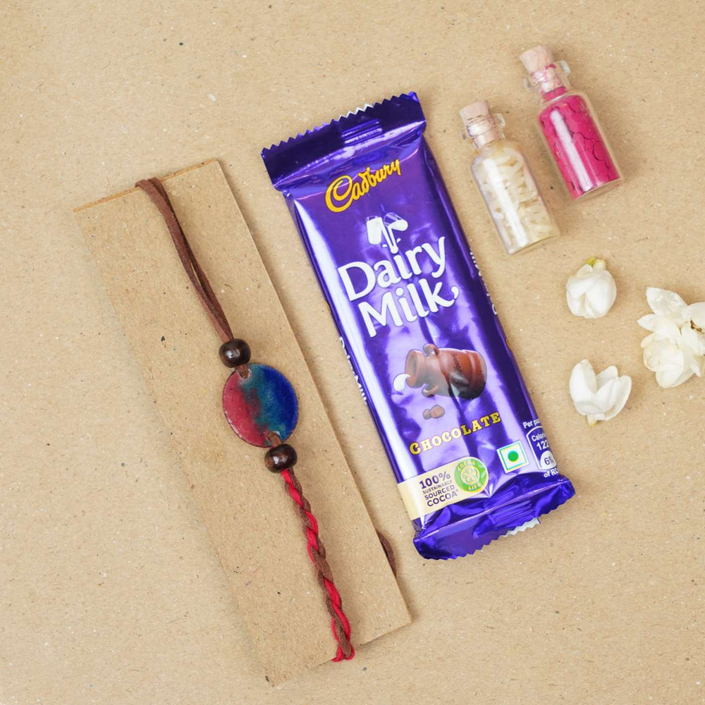 Handmade Rudra Red Copper Enamel Rakhi With Chocolates And Roli Chawal - Flat Lay with Bracelet and Chocolate