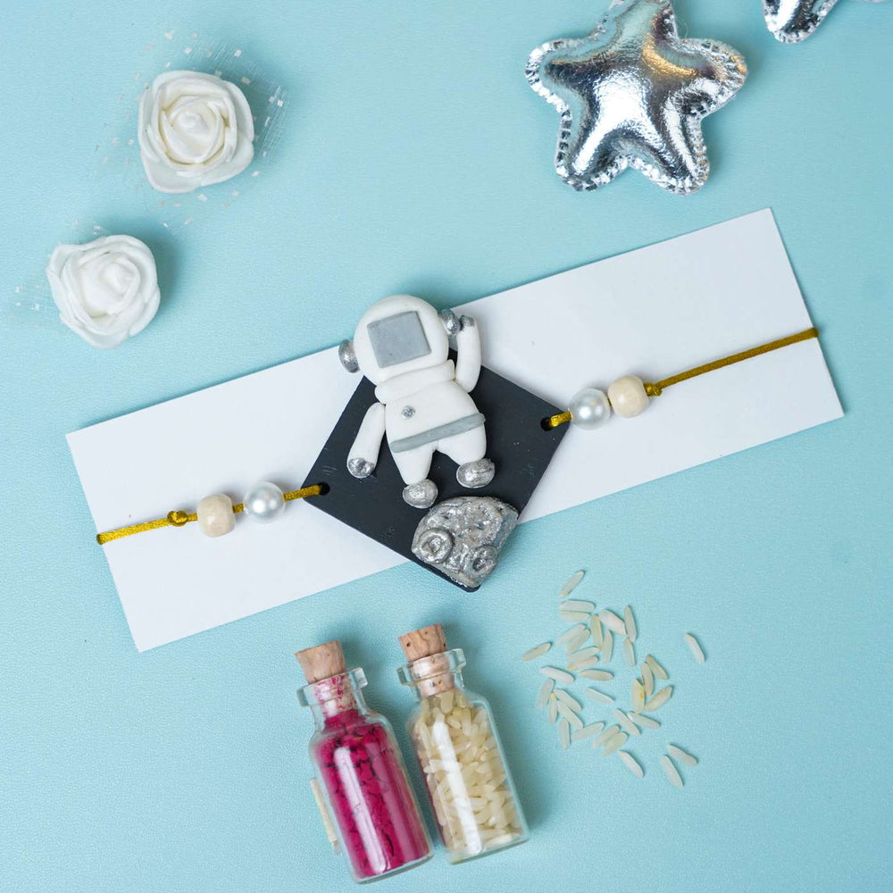 Handmade Miniature Clay Astronaut Kids Rakhi With Roli Chawal - Flat Lay with Astronaut Charm Card