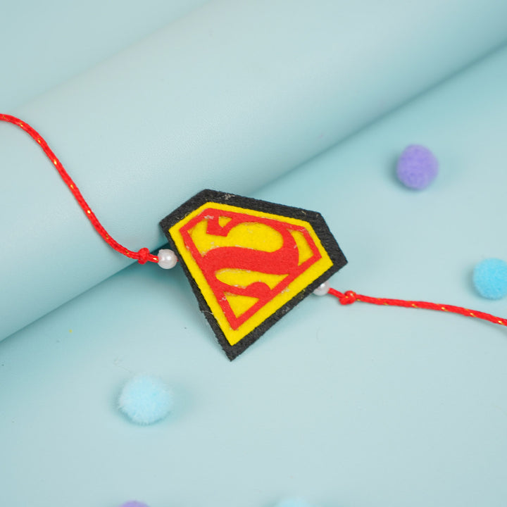 Handmade Beaded Superman Theme Pom Pom Felt Rakhi With Roli Chawal For Kids - Close-up of Rakhi charm