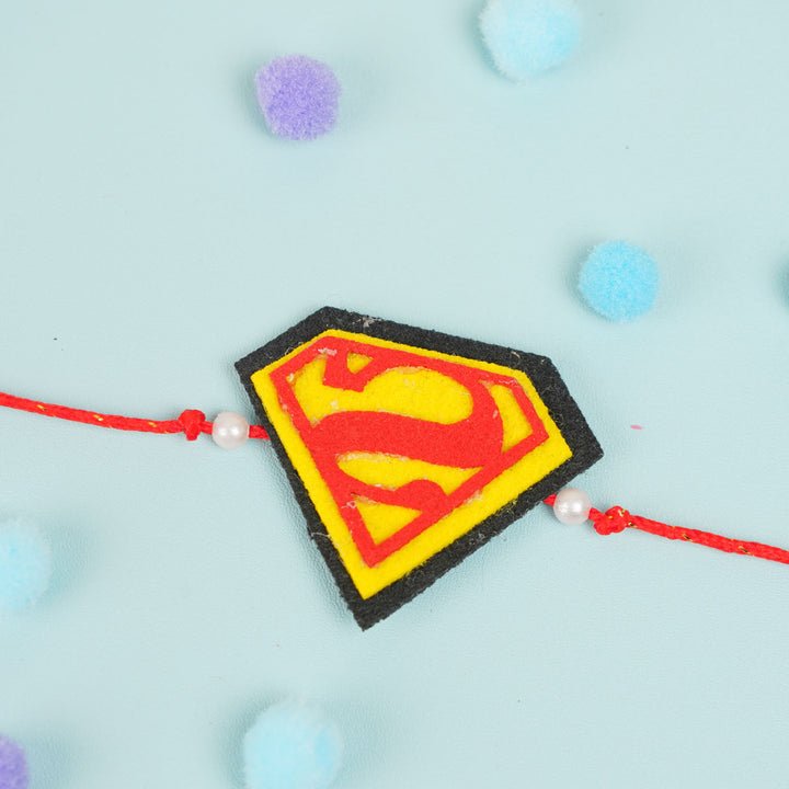 Handmade Beaded Superman Theme Pom Pom Felt Rakhi With Roli Chawal For Kids - Top-down view of Rakhi
