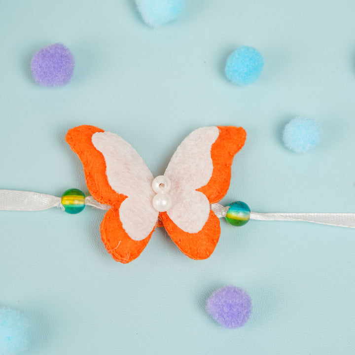 Customized Handmade Beaded Butterfly Theme Pom Pom Felt Rakhi With Roli Chawal For Kids - Top View with Symmetrical Layout