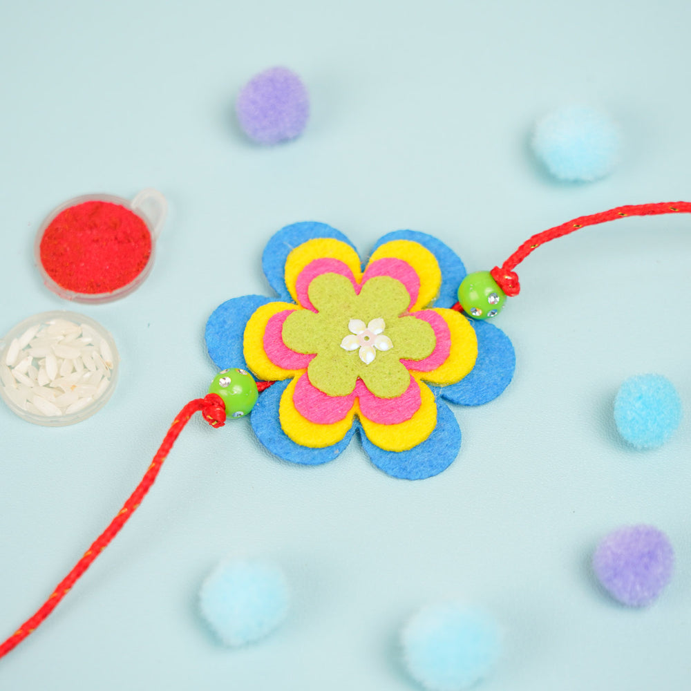 Handmade Beaded Flower Theme Pom Pom Felt Rakhi With Roli Chawal For Kids - Flat Lay with Decorative Items