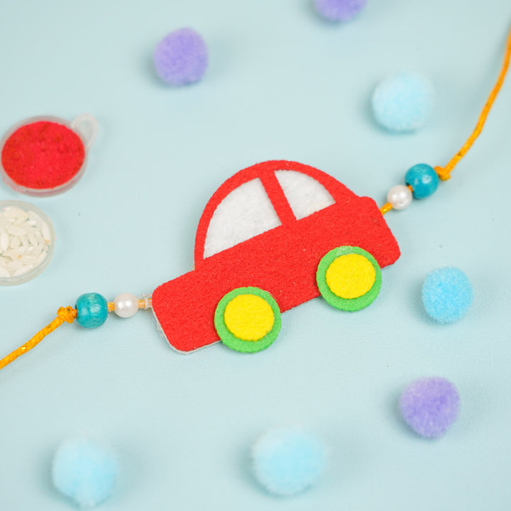 Customized Handmade Beaded Car Theme Pom Pom Felt Rakhi With Roli Chawal For Kids - Top view of red car charm