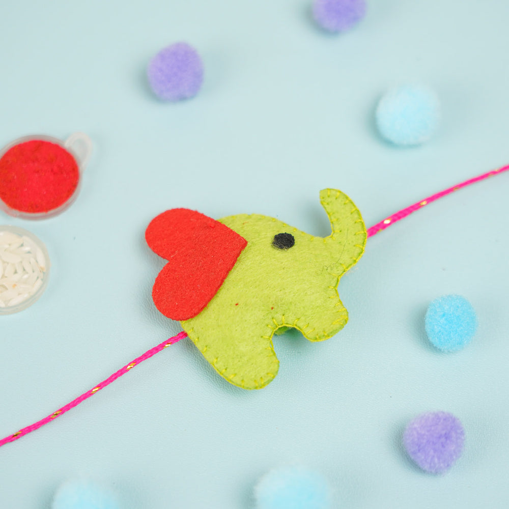 Customized Handmade Beaded Elephant Theme Pom Pom Felt Rakhi With Roli Chawal For Kids - Side View of Green Elephant Charm