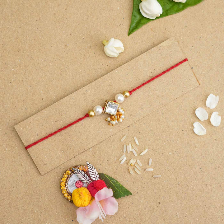 Handmade Kundan Diamond Shape Rakhi With Roli Chawal - Flat lay with accessory on card