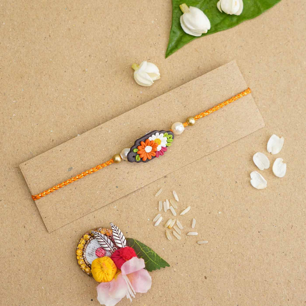 Handmade Miniature Clay Orange And White Floral Rakhi With Roli Chawal - Laid flat on packaging card