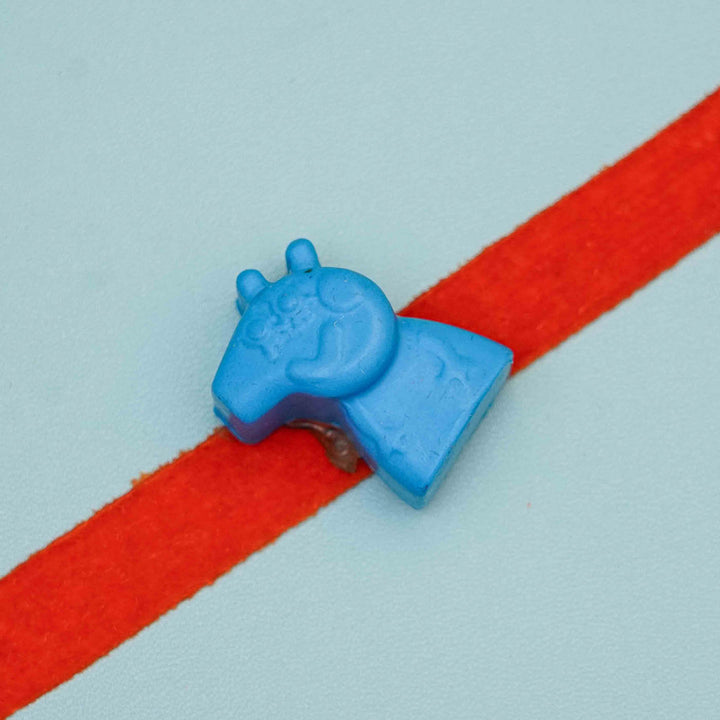 Handmade Peppa Pig Crayon Kids Rakhi With Roli Chawal - Close-up of blue clip on red band