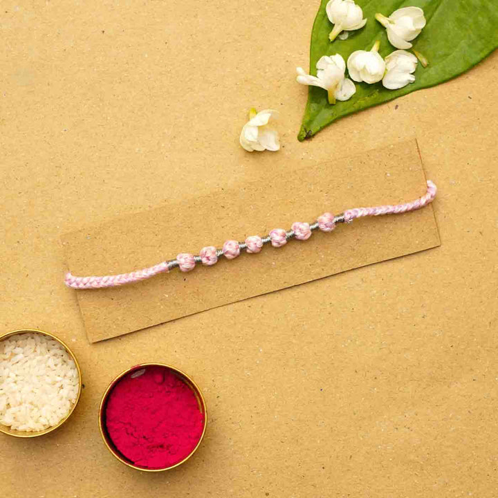 Reusable Beaded Pink Ombre Knot Rakhi With Roli Chawal - Flat lay with festive elements
