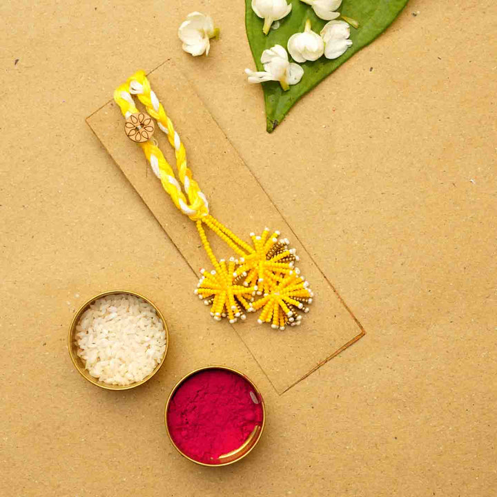 Reusable Beaded Yellow Flower Lumba Rakhi For Bhabhi With Roli Chawal - Flat lay with traditional items