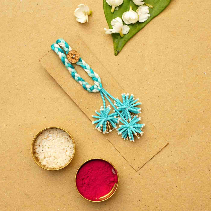 Reusable Beaded Blue Flower Lumba Rakhi For Bhabhi With Roli Chawal - Flat lay with traditional materials